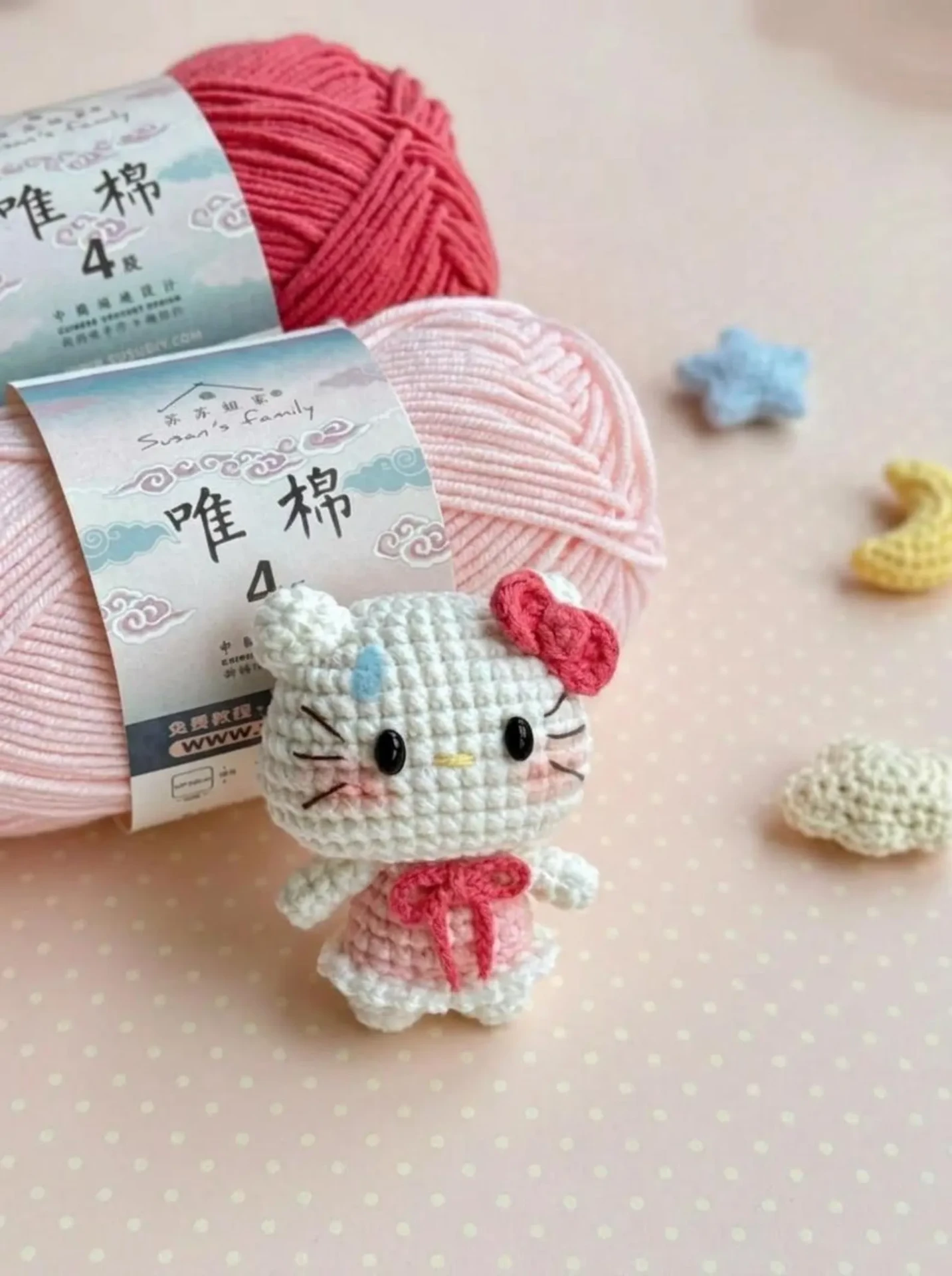 White crochet kitty keychain in a pink dress beside pink and coral yarn balls