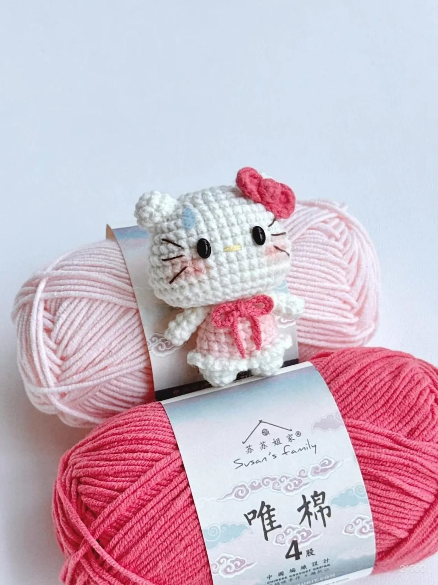 Crochet kitty keychain resting between two balls of yarn
